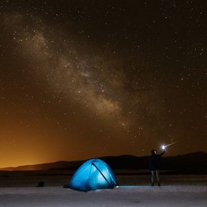 Young man standing by illuminated tent against star field at night