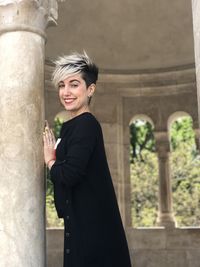 Smiling young woman standing against built structure