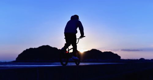 Full length of man cycling at beach against sky during sunset