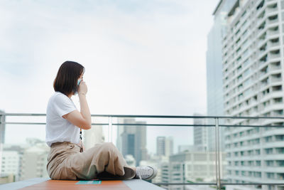 Solo asian woman wear protective mask during outdoor break and relax at rooftop with city background