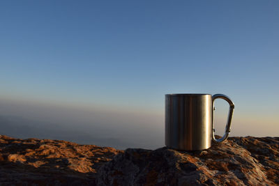 Coffee cup on rock against clear blue sky