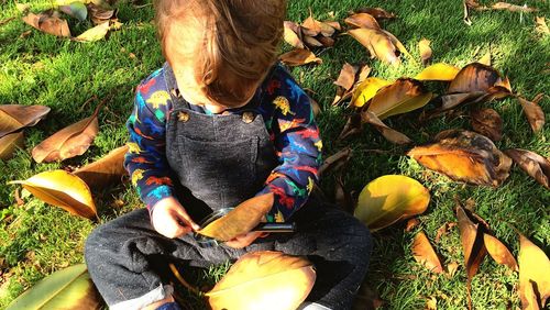 High angle view of baby boy with leaves sitting on land in park during autumn