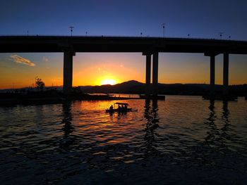 Silhouette bridge over river against sky during sunset