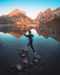 Man standing on rock by lake against sky