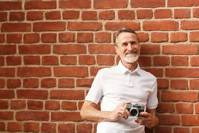 Portrait of a man holding camera against brick wall