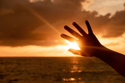 Cropped image of hand against sky during sunset