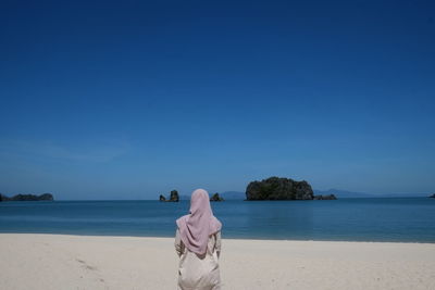 Rear view of woman on beach against clear blue sky