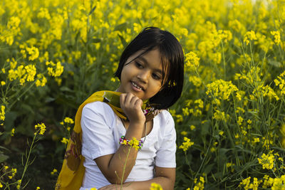 A beautiful innocent indian girl child in white dress sitting near yellow mustard flower field