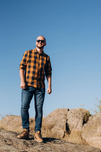 Young man standing on rock against clear blue sky