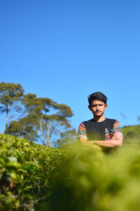 Portrait of boy against plants against clear blue sky