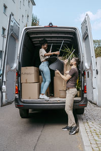 Multiracial couple assisting each other while unloading chair from van trunk