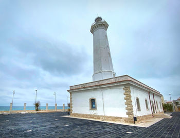 View of lighthouse by building against sky