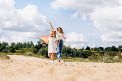 A laughing little girl and her mother run along the road to the field and fly a kite.