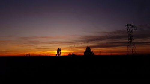 Silhouette electricity pylons on field against sky during sunset