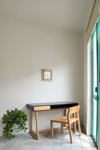 Wooden desk with chair, plants in the room, natural sunlight coming in, pasta tile floor, white 