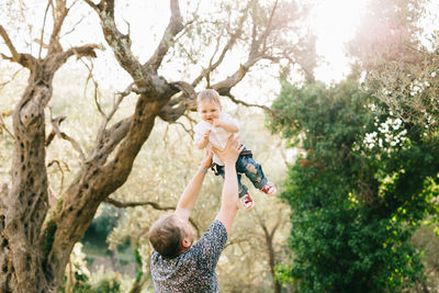 Rear view of father holding baby tree against plants