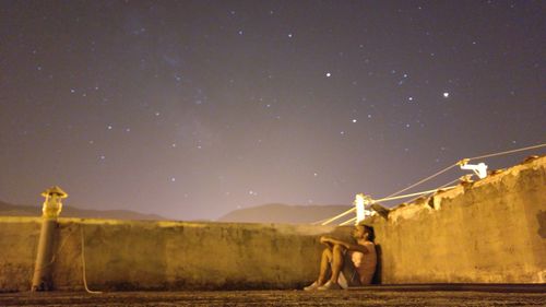 Man sitting on building terrace against star field at night