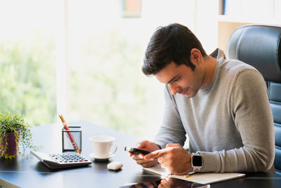 Young man using mobile phone while sitting on table