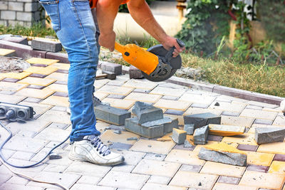 A worker using an electric angle grinder and stone cutting disc cuts paving slabs during the repair.
