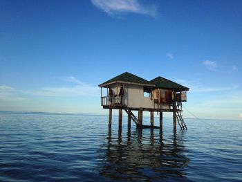 Stilt house on sea by building against sky