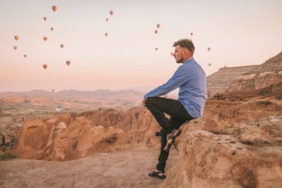 Side view of young man standing on rock against sky