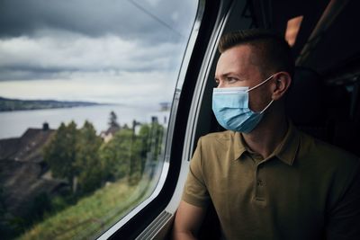 Man wearing mask looking through window in train