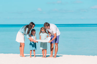 Full length of family standing on beach against sky