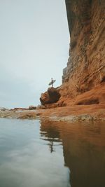 Low angle view of mid adult man with surfboard standing on rock formation at beach against sky