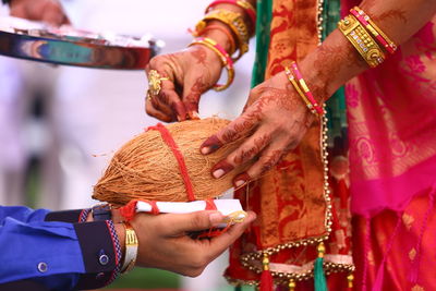 Close-up of couple holding coconut and fabric during religious event