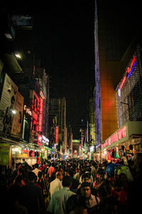 People on illuminated street amidst buildings at night