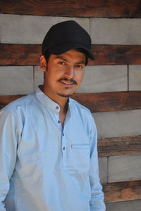 Waist up of a young guy with wearing cap, looking at camera while staging against wall