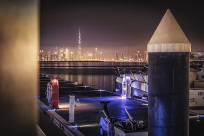 Illuminated buildings by sea against sky at night