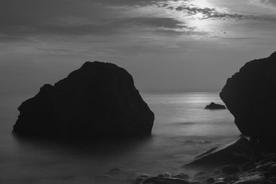 Rock formation in sea against sky in black and white