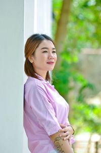 Smiling young woman looking away while standing by wall