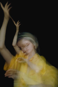 Portrait of young woman with hands against black background