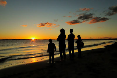 Silhouette people standing at beach against sky during sunset