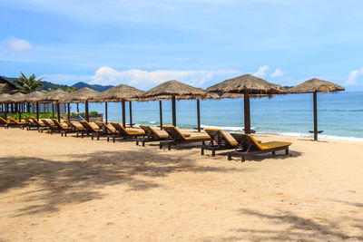 Deck chairs on beach against sky