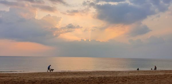 People on beach against sky during sunset