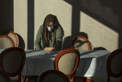 Man with dreadlocks wearing mask while sitting at table