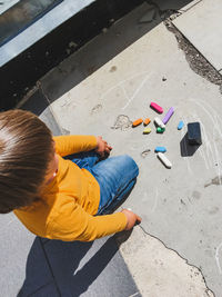 Toddler in jeans draws with crayons on asphalt. kid's hands,clothes are covered with colorful stains