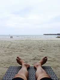 Low section of person relaxing on beach against sky