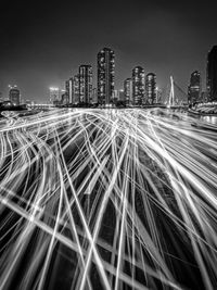 Light trails on street amidst buildings against sky at night