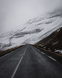 Road leading towards snowcapped mountain against sky