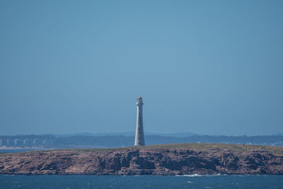 Lighthouse by sea against clear blue sky