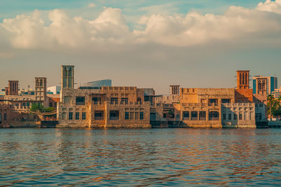 Buildings by river against sky during sunset