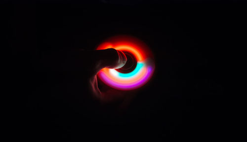 Cropped image of hand holding illuminated fidget spinner over black background