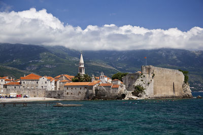 Buildings at waterfront against cloudy sky