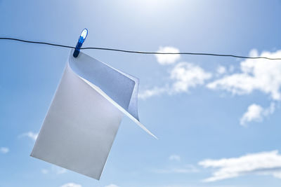 Close-up of paper hanging from clothespin on string against blue sky