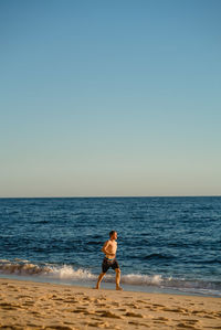 Shirtless man walking on shore at beach