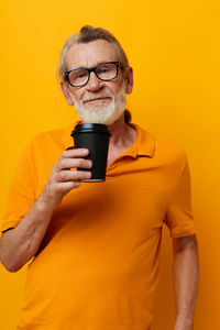 Portrait of senior man drinking coffee against yellow background